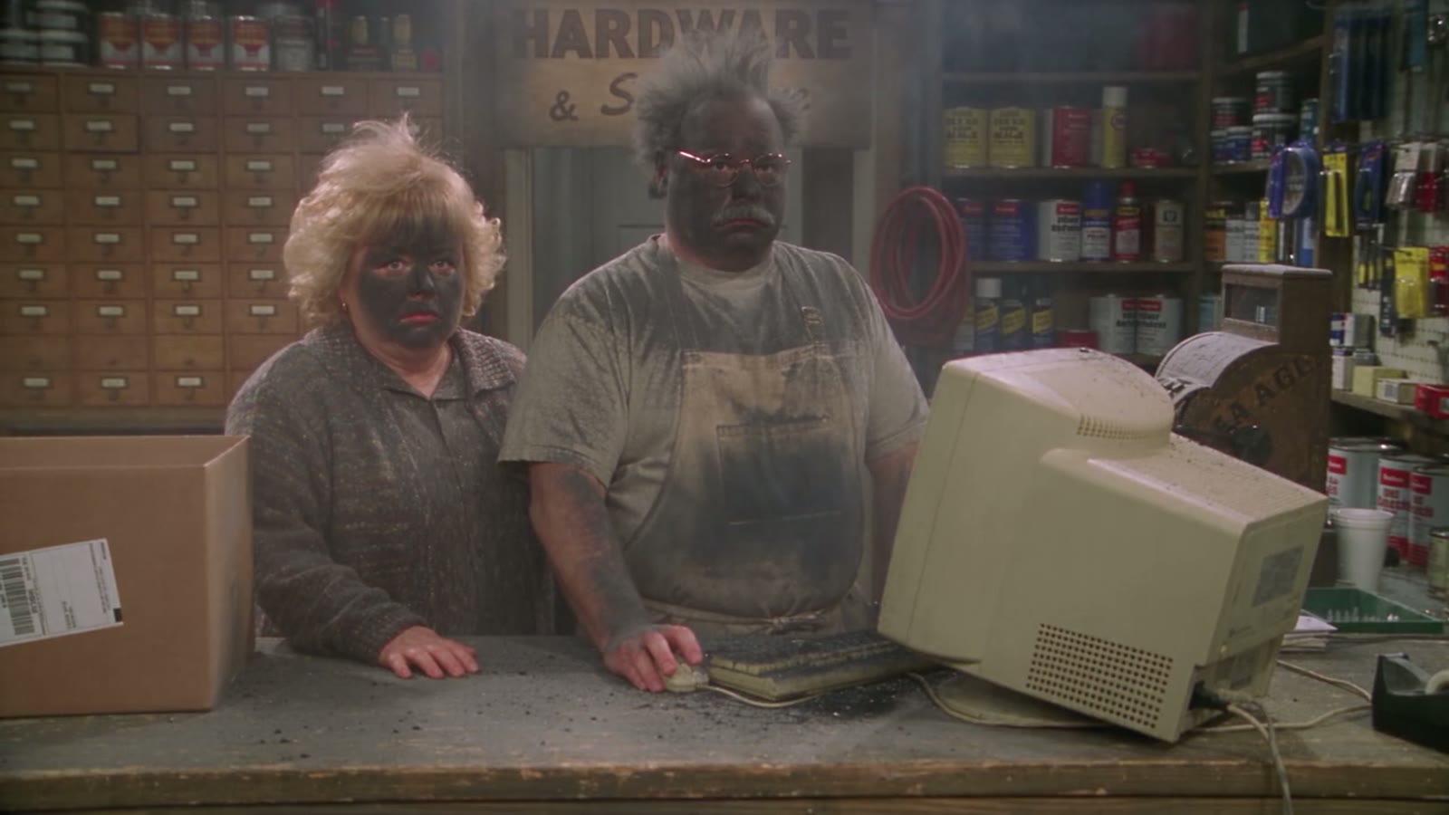 Gary und Linda stehen rußgeschwärzt hinter der Ladentheke, daneben der ausgebrannte Rechner
